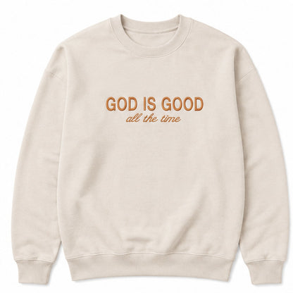 A cream-colored crewneck sweatshirt with the text 'GOD IS GOOD all the time' printed on the chest in a warm brown color, displayed against a solid white background.